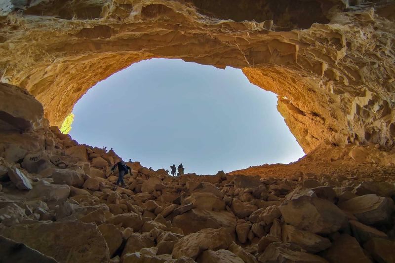 The wide opening of Heet Cave seen from inside, with visitors on the rock slope